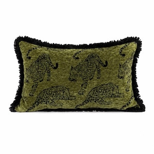 Puede incluir: Un cojín rectangular de tela verde oliva texturizada con un patrón repetitivo de leopardos negros. El cojín está rematado con un grueso borde de flecos negros a lo largo de sus cuatro lados, creando un contorno bien definido.
