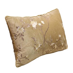 May include: A rectangular, gold cushion with an embroidered floral design. The embroidery features white and light brown flowers and stems. The cushion has a gold border and is made of a soft, velvety material.