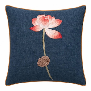 Puede incluir: Cojín cuadrado azul marino con un diseño de flor de loto bordada. La flor es rosa y blanca con puntas rojas, y el tallo es verde. El cojín tiene un borde marrón.