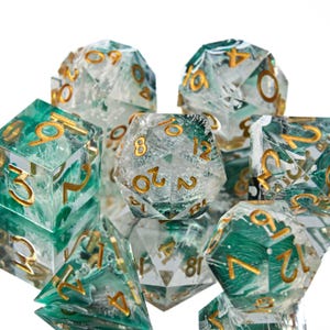 May include: A collection of polyhedral dice with a clear, marbled appearance, featuring swirls of green and white. The numbers are in gold. The dice are designed for tabletop role-playing games.