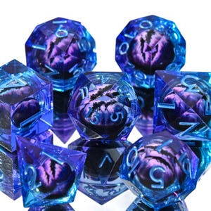 May include: A set of polyhedral dice in shades of blue and purple. The dice have a faceted design with visible numbers and internal artwork. The dice are designed for tabletop role-playing games.