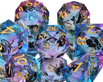 Puede incluir: Un conjunto de dados poliédricos de varias formas. Los dados son una mezcla de azul, morado y transparente, con números dorados e ilustraciones de murciélagos negros. Para juegos de mesa.