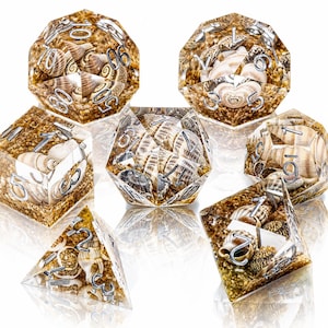 May include: A set of seven polyhedral dice made of clear resin, each containing small seashells and golden sand particles. The dice feature silver-colored numbers etched into the surfaces, including a d20, d12, d10, d8, d6, d4, and a percentile die.