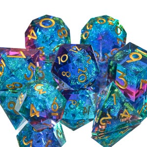 May include: A collection of iridescent polyhedral dice in blue, purple, and gold. The dice are made of a clear, crackled material with gold numbering. The set includes various shapes for role-playing games.