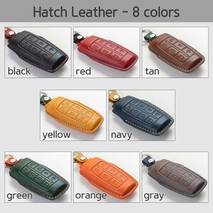 Op de afbeelding: Een verzameling van acht lederen sleuteletuis in verschillende kleuren: zwart, rood, bruin, geel, marineblauw, groen, oranje en grijs. Elke hoes heeft een getextureerd oppervlak en een knoppenindeling. De tekst "Hatch Leather - 8 kleuren" staat bovenaan.