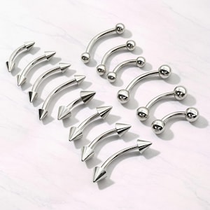 Puede incluir: Una colección de joyas para piercing de cejas curvas. Las joyas son de metal plateado. Algunas piezas tienen una bola en cada extremo, otras una punta cónica.