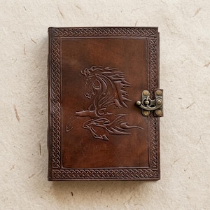 May include: A brown leather journal with a raised horse design on the cover. The journal has a decorative border and a metal clasp. The leather is a rich, dark brown color.
