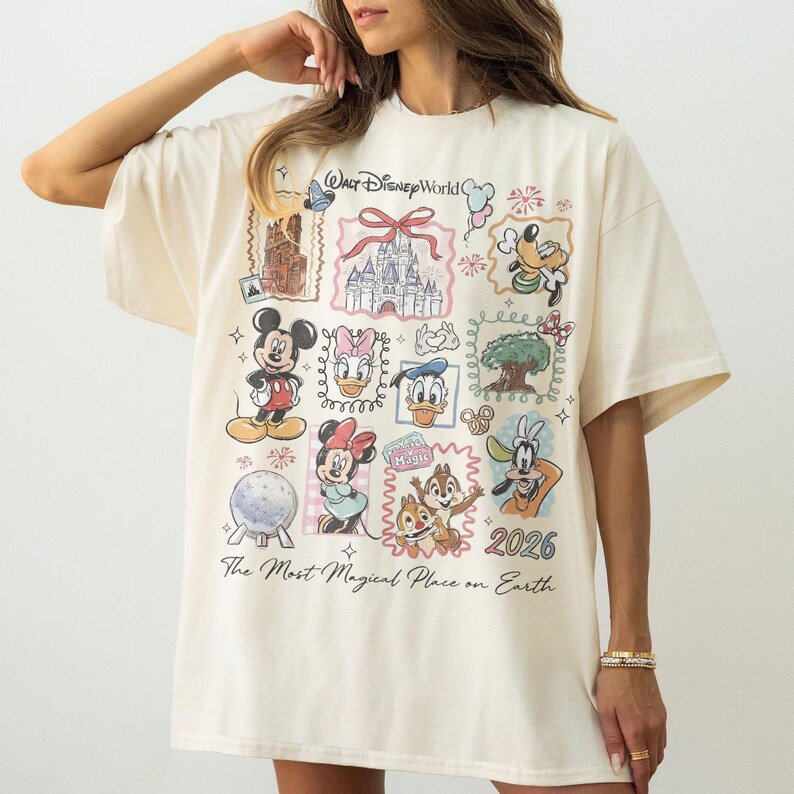 May include: Cream-colored t-shirt featuring a collage of Disney characters and landmarks. The design includes Mickey Mouse, Minnie Mouse, Donald Duck, and Goofy, along with the text "Walt Disney World" and "2026". The shirt also has the phrase "The Most Magical Place on Earth".
