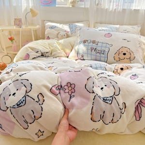 Peut inclure: Une parure de lit crème avec des illustrations de chiens de dessin animé, des fleurs et les mots "FREE TIME". L'ensemble comprend une housse de couette et des oreillers. La housse de couette a un motif floral rose et blanc.