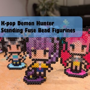 Puede incluir: Figuras de cuentas de fusibles de pie al estilo de los personajes de K-pop Demon Hunter. Las figuras están hechas de cuentas de plástico de colores, con una variedad de colores que incluyen rosa, morado, negro y azul. Las figuras están sobre una superficie de madera.