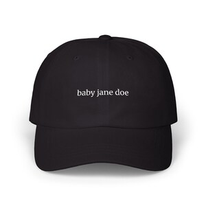 Könnte beinhalten: Schwarze Baseballkappe mit dem weißen Text "baby jane doe" mittig auf der Vorderseite. Die Kappe hat einen gebogenen Schirm und eine strukturierte Krone. Ein lässiges Accessoire.