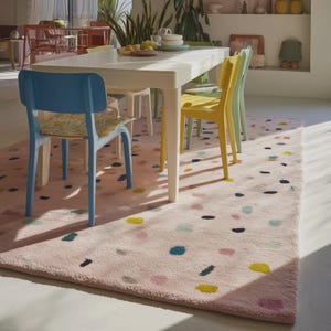 May include: A light pink rug with a pattern of colorful, irregular shapes in yellow, blue, green, and black. The rug is placed under a white dining table and colorful chairs, creating a vibrant and inviting dining area.