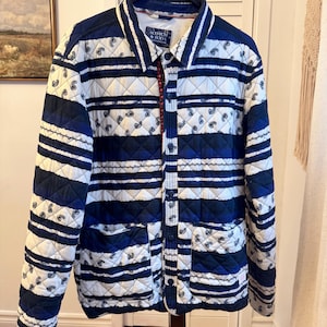 Op de afbeelding: Gewatteerde jas met een wit en marineblauw paisley- en streepmotief. De jas heeft een kraag, twee voorzakken en een knoopsluiting. De merknaam "SCOTCH & SODA" is zichtbaar.