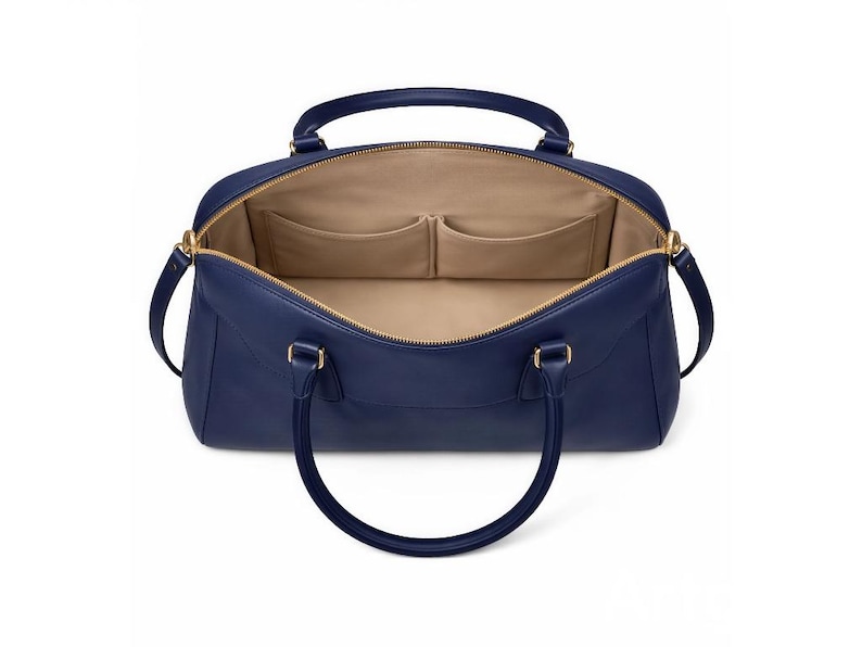 May include: Open navy blue leather handbag with gold-tone hardware. The interior features two pockets and a beige lining. The bag has two handles and a zipper closure.