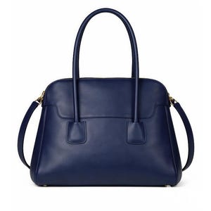 May include: A navy blue leather handbag with a structured design. The bag features two top handles and a detachable shoulder strap. Gold-toned hardware accents the zipper and strap attachments. The bag is approximately 12 inches wide.