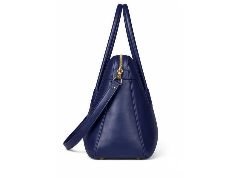 May include: A navy blue tote bag with a gold zipper and handles. The bag has a shoulder strap and a structured design. The bag is made of a smooth material and has a classic, elegant look.