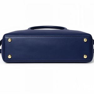 May include: A navy blue handbag with a top handle and a detachable shoulder strap. The bottom of the bag features four gold-colored feet. The bag has a rectangular shape and a smooth, leather-like texture.