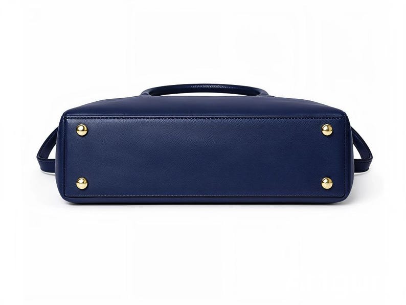 May include: A navy blue handbag with a top handle and a detachable shoulder strap. The bottom of the bag features four gold-colored feet. The bag has a rectangular shape and a smooth, leather-like texture.