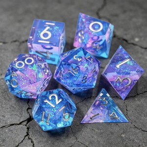 Op de afbeelding: Set van zeven polyhedrale dobbelstenen in verschillende vormen. De dobbelstenen zijn transparant blauw met ingebedde iriserende glitter en zilveren cijfers. De set bevat een d4, d6, d8, d10, d12, d20 en een percentieldobbelsteen, voor tabletopspellen.