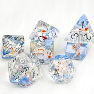 May include: A collection of clear, multi-sided dice with a blue and orange fish theme. The dice are transparent, with visible numbers and small, colorful fish suspended inside. The dice are arranged on a white surface.