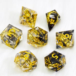 May include: Set of seven polyhedral dice with a clear resin base, gold-colored accents, and yellow numbering. The dice feature intricate designs and are suitable for tabletop gaming. The dice are in various shapes, including a d4, d6, d8, d10, d12, d20, and a percentile die.