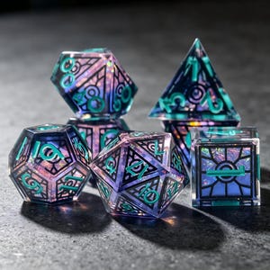 May include: A set of polyhedral dice featuring a clear resin construction with an internal iridescent shimmer. Each die has black geometric line patterns and bright teal numbers. The set includes a d20, d12, d10, d8, and a d4, all displaying sharp edges and a translucent finish that catches the light.