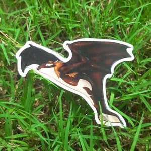 May include: A black and white sticker of a dragon with brown wings flying in the air. The dragon is in a cartoon style and has a white belly.