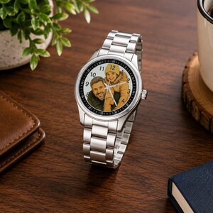 Puede incluir: Un reloj de pulsera anal&oacute;gico de tono plateado con una correa de eslabones met&aacute;licos. La esfera del reloj presenta una fotograf&iacute;a en color personalizada de un adulto y un ni&ntilde;o con un gorro amarillo. La esfera tiene n&uacute;meros ar&aacute;bigos negros.