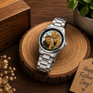 Puede incluir: Un reloj anal&oacute;gico de tono plateado con una esfera de foto personalizada que muestra a una persona y un ni&ntilde;o. El reloj tiene una correa de eslabones de acero inoxidable, una esfera redonda con n&uacute;meros negros y manecillas plateadas. Se presenta junto a una caja de madera con texto grabado y una etiqueta de papel marr&oacute;n que dice Happy Father's Day.