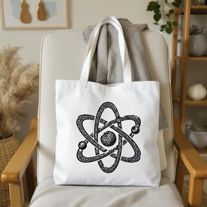 May include: White tote bag with a black atom symbol design. The bag has a clean aesthetic, with the graphic centered on the front. The handles are white, and the bag appears to be made of a sturdy fabric.
