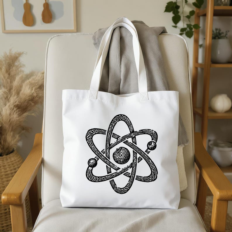 May include: White tote bag with a black atom symbol design. The bag has a clean aesthetic, with the graphic centered on the front. The handles are white, and the bag appears to be made of a sturdy fabric.