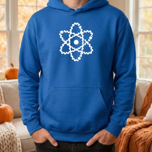 May include: Royal blue hoodie featuring a white atom graphic. The hoodie has a front pocket and a drawstring hood. The atom graphic is a stylized representation of an atom's structure.