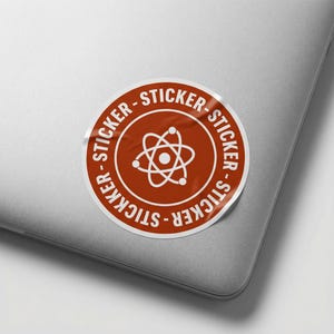 May include: A circular sticker with a white border and a rust-coloured centre. The centre features a white atom symbol. The words "STICKER" are printed in white around the edge of the sticker. The sticker is on a grey laptop.