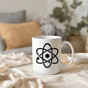 May include: White ceramic mug with a black atom symbol. The mug has a curved handle and is filled with a hot drink, with steam rising. The mug is on a white surface. The mug is likely 10-12 cm tall.