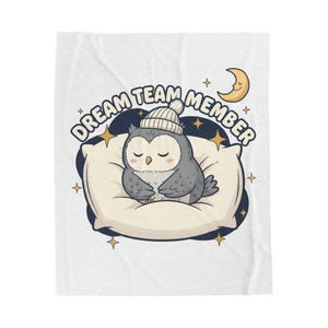 May include: A white blanket featuring a cartoon owl wearing a knit cap, resting on a pillow. The text "DREAM TEAM MEMBER" is arched above the owl. A crescent moon and stars are also present in the design.