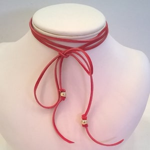 May include: A red leather choker necklace with two gold beads. The necklace is tied in a bow at the front.
