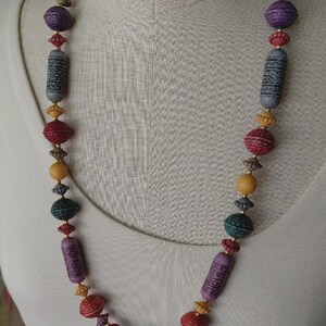 May include: A vibrant beaded necklace with a mix of bead shapes and sizes. The necklace showcases beads in purple, red, green, yellow, and grey hues. Some beads are cylindrical with etched patterns, while others are round or oval.