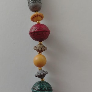 May include: A necklace featuring a variety of beads in red, green, yellow, and grey. The beads have diverse shapes and textures, with gold-coloured accents. The top bead is cylindrical and grey, while the others are spherical or flower-shaped.