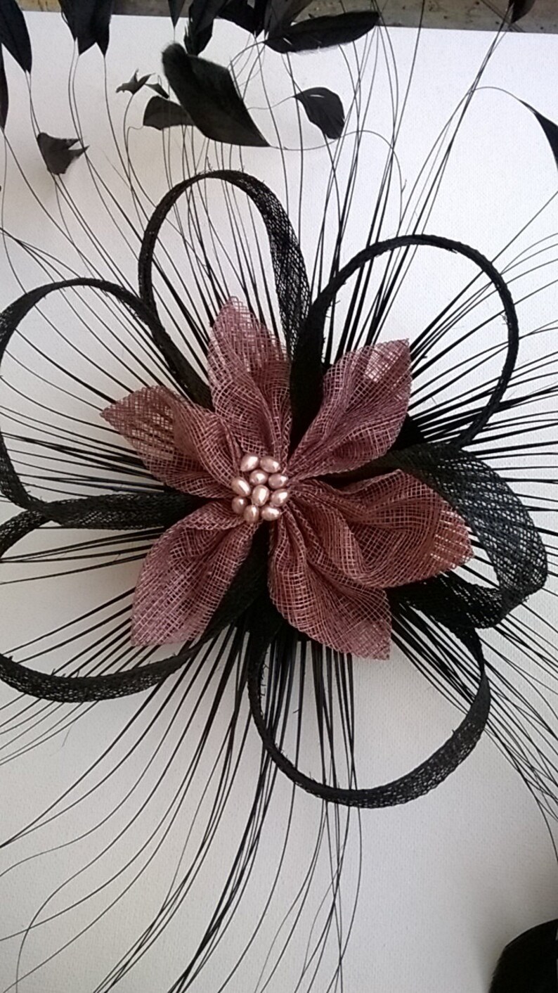 May include: A black feather hair comb with a pink flower accent. The flower has a pearl center.
