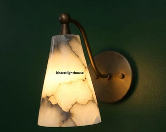 May include: A wall sconce with a conical, off-white shade featuring gray veining. The sconce has a curved, dark bronze arm and a circular mounting plate. The text "bharatlighthouse" is visible on the shade.