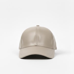 Könnte beinhalten: Taupefarbene Baseballkappe mit gebogenem Schirm. Die Kappe hat ein strukturiertes Design mit einem oberen Knopf und einer glatten, einfarbigen Oberfläche. Das ist ein neutrales Accessoire.