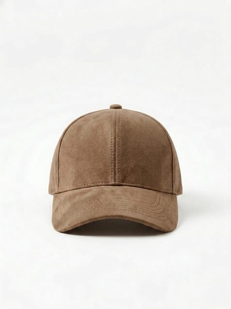 K&ouml;nnte beinhalten: Braune Baseballkappe mit gebogenem Schirm. Die Kappe besteht aus einem Wildleder-&auml;hnlichen Material und hat eine strukturierte Krone. Sie hat einen kleinen Knopf oben und eine Naht in der Mitte.