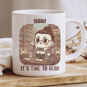 Puede incluir: Taza de cerámica blanca con un personaje de bibliotecario de dibujos animados con gafas y pajarita, en un escenario de biblioteca. La taza presenta el texto "SHHH! IT'S TIME TO READ". La taza tiene un asa curva. La ilustración es de estilo caricaturesco.