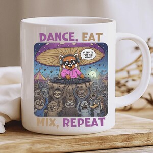 Puede incluir: Taza de cerámica blanca con una ilustración de dibujos animados de un panda rojo pinchando bajo una seta. El diseño incluye el texto "DANCE, EAT, MIX, REPEAT" y un bocadillo que dice "SLEEP IS FOR THE WEAK!"