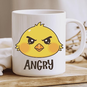 Puede incluir: Taza de cerámica blanca con un dibujo de un pollito amarillo enfadado. El pollito tiene ojos negros, mejillas naranjas y un pico. La palabra "ANGRY" está impresa en negro debajo.