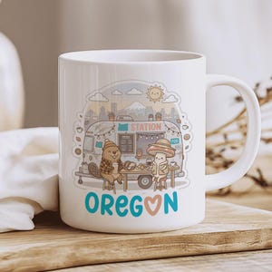 Könnte beinhalten: Weißer Keramikbecher mit einer Cartoon-Illustration einer Imbisswagen-Szene, mit einem Biber und einer Pilzfigur. Der Becher zeigt das Wort "OREGON" in Türkis und Rosa, mit einem Herzsymbol. Das Design umfasst eine Sonne, Wolken und einen Berg.