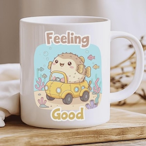 Puede incluir: Taza de cerámica blanca con un pez globo de dibujos animados conduciendo un coche amarillo bajo el agua. La taza tiene las palabras "Feeling Good" en una fuente lúdica. El diseño incluye peces, corales y burbujas.