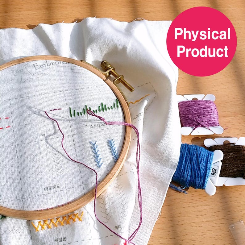 May include: Embroidery hoop with white fabric featuring various stitch patterns and the word "Embroidery". Spools of purple, blue, and brown embroidery floss are visible. The wooden hoop is secured with a brass clasp.