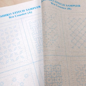 May include: Two sheets of light-colored fabric printed with blue Sashiko stitch sampler patterns for tea coasters. The left sheet is labeled Sashiko Stitch Sampler Tea Coaster (A) and the right sheet is labeled Sashiko Stitch Sampler Tea Coaster (B).