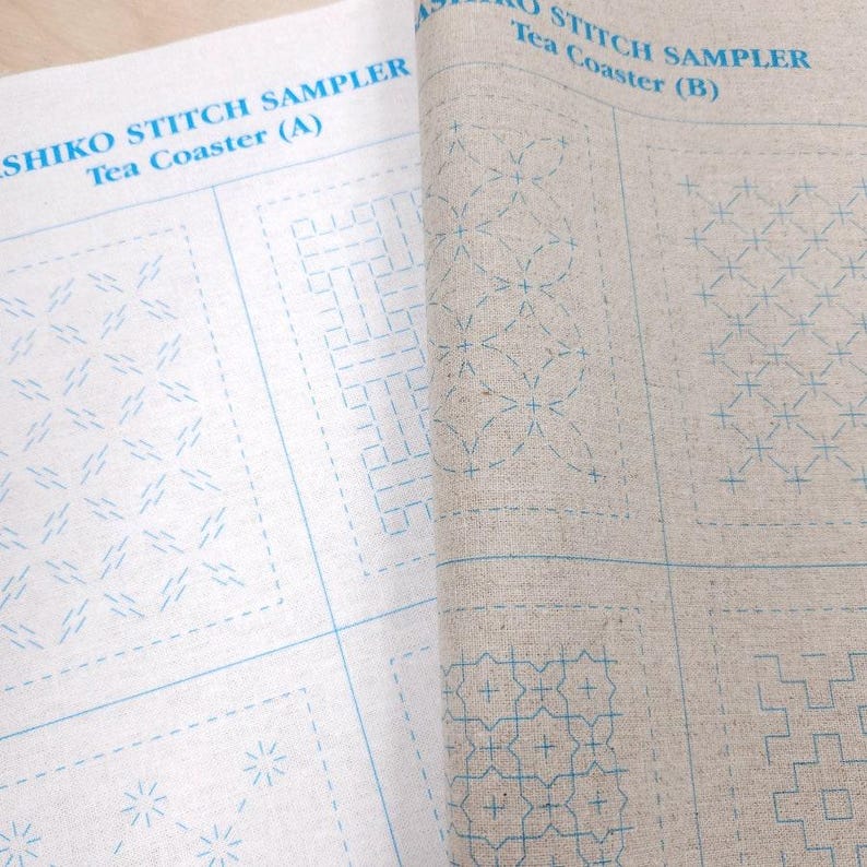 May include: Two sheets of light-colored fabric printed with blue Sashiko stitch sampler patterns for tea coasters. The left sheet is labeled Sashiko Stitch Sampler Tea Coaster (A) and the right sheet is labeled Sashiko Stitch Sampler Tea Coaster (B).